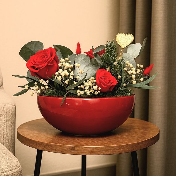 A glossy red bowl filled with preserved red roses, and plants