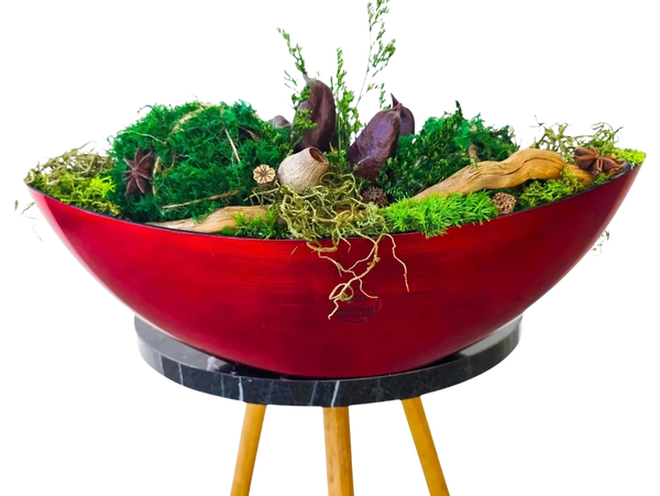 Red boat-shaped filled with a arrangement of green moss, leaves, star anise, pieces of driftwood.