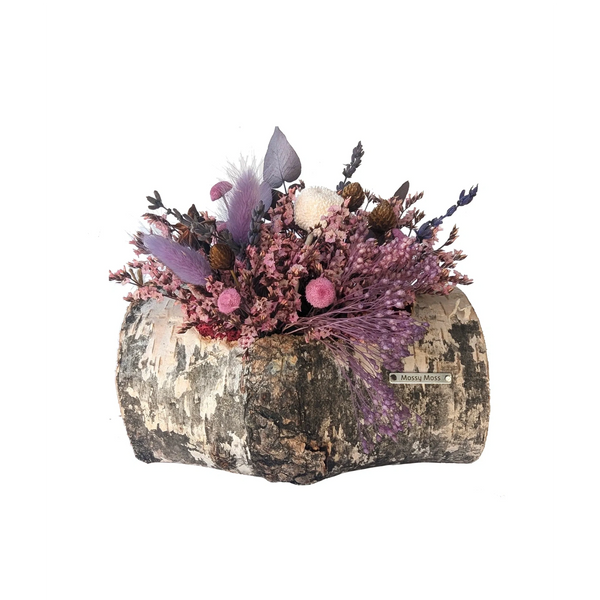 A cylindrical birch bark planter holds a delicate arrangement of preserved plants  in shades of pink