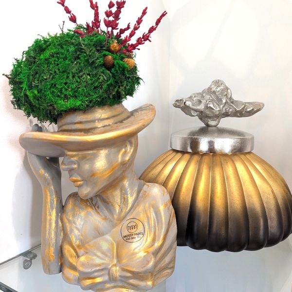 Silver/gold pot, person wearing a wide hat filled with green moss and red levanda.