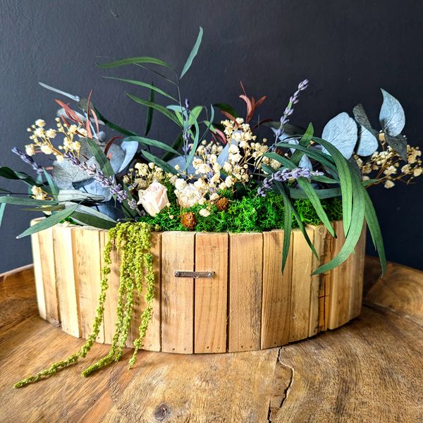 A round wooden planter from vertical slats, filled with mos delicate white roses & plants