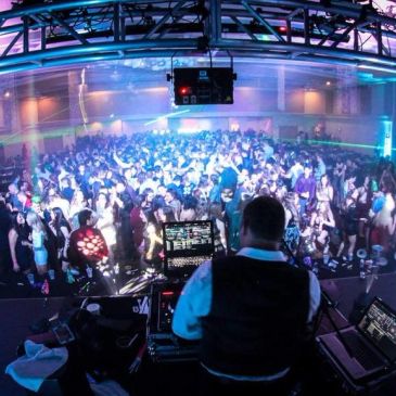 DJ performing for a large, vibrant crowd at a packed nightclub.