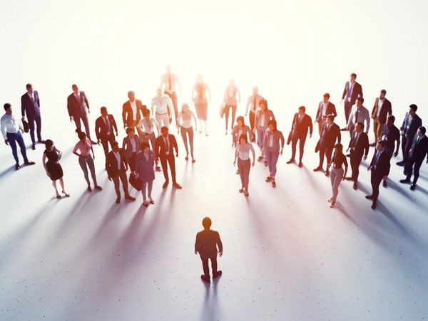 A lone figure faces a large group of professionals in a bright, spacious setting.