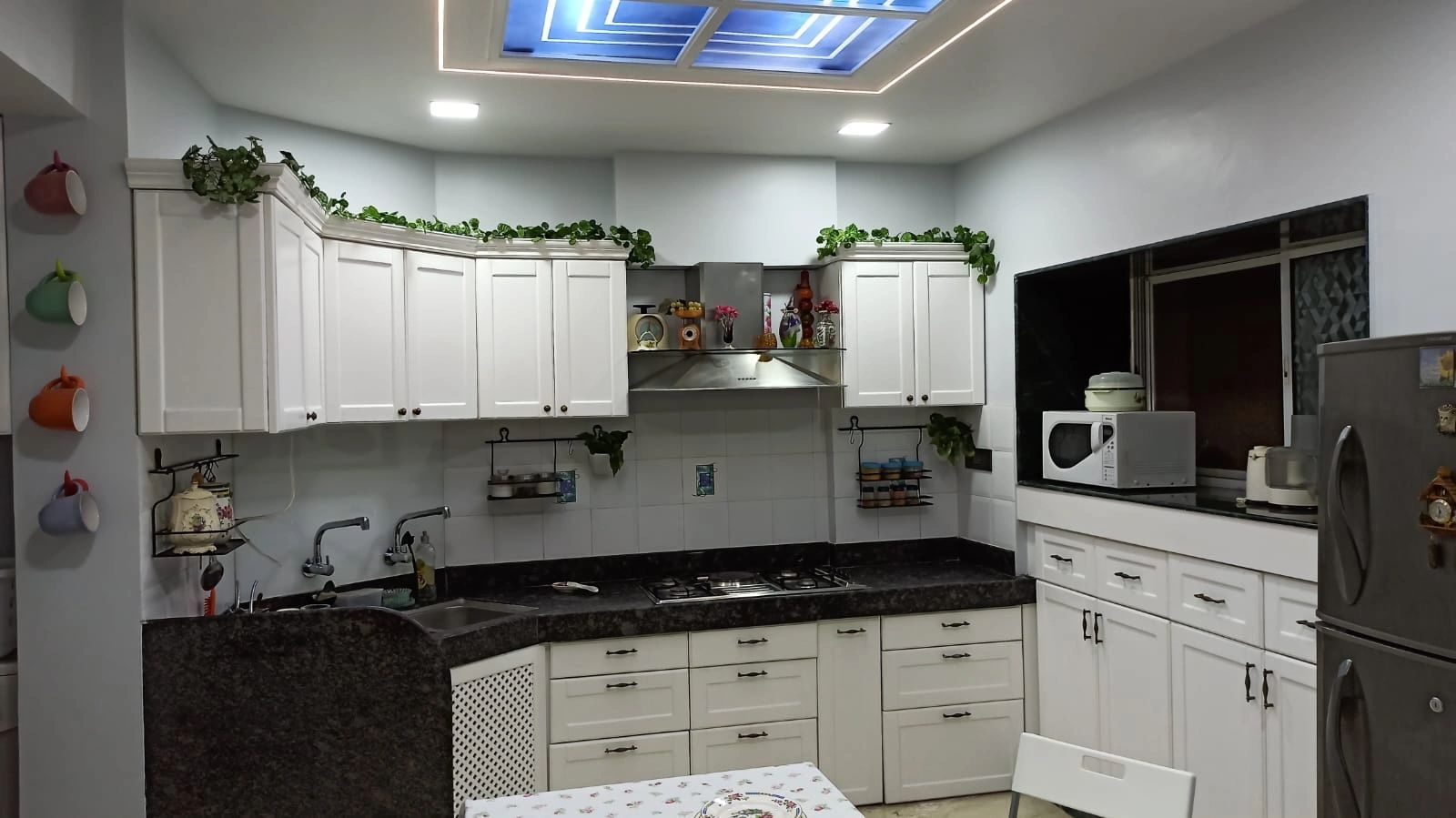 Modern kitchen with white cabinets, black countertops, and colorful mugs on the wall.
