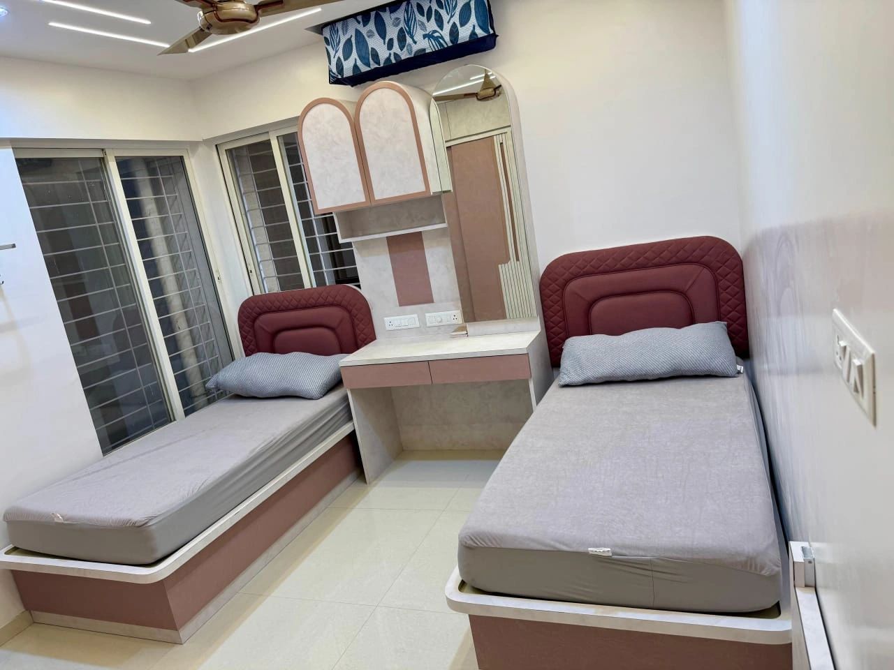 A clean, modern twin bedroom with two single beds and a central vanity.