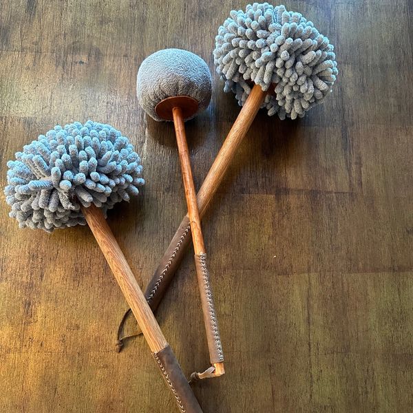 Three drum mallets with different textured heads on a wooden surface.