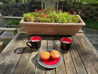 Two muffins and two cups of coffee on a wooden table outdoors.