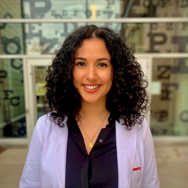 Smiling woman with curly hair in a white coat.