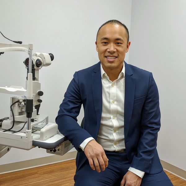 Man in a blue suit sitting beside eye examination equipment.