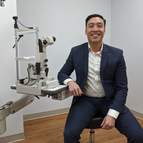 Man in suit sitting next to eye exam equipment.