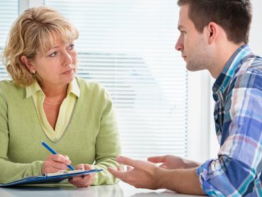 A mature woman listens intently while taking notes during a discussion with a man.