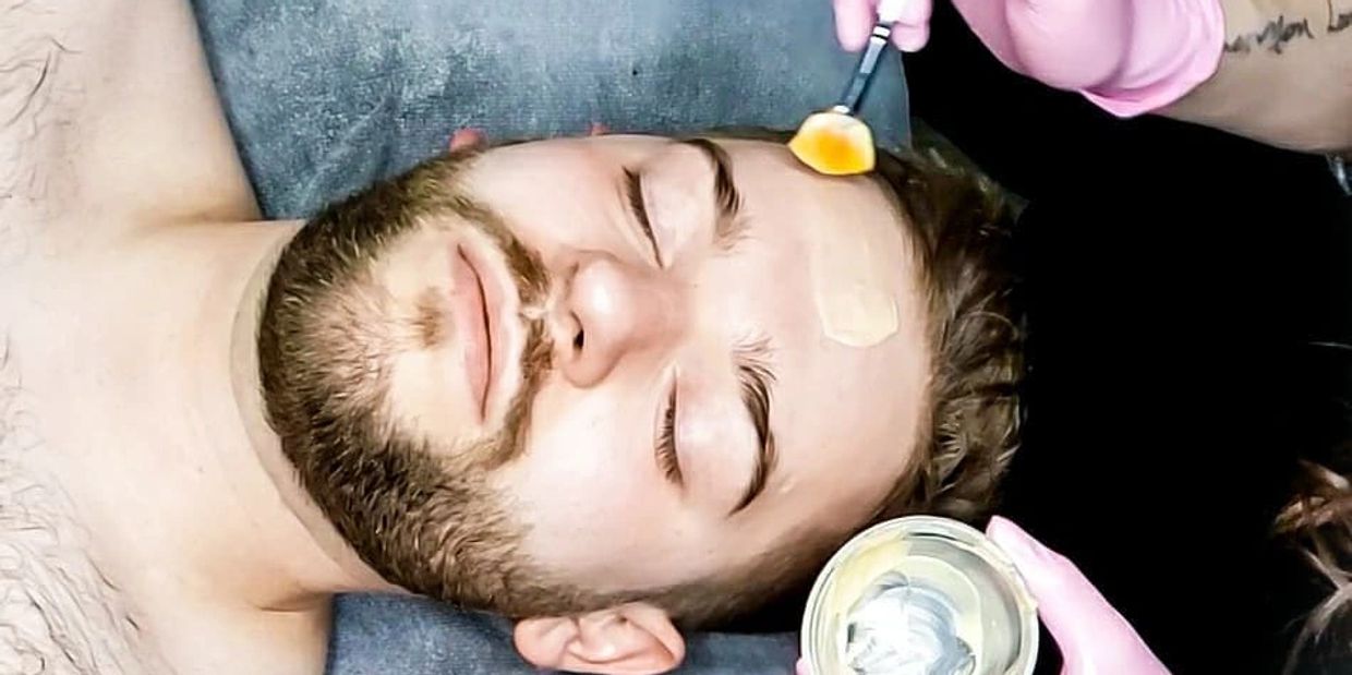 A bearded man getting a Facial Treatment, an orange treatment mask is being applied to his forehead