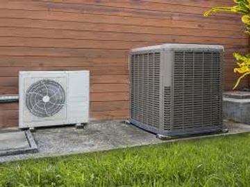Two outdoor air conditioning units installed beside a wooden wall.