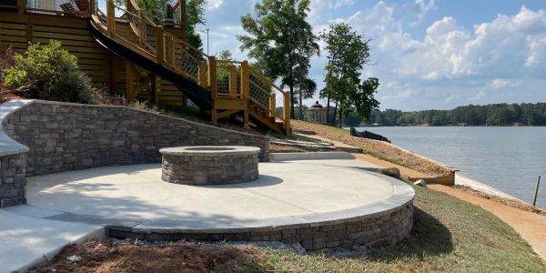 Stone fire pit on a curved concrete patio overlooking a lake.