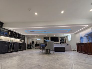 Modern basement with sleek kitchen, dining area, and ambient blue ceiling lights.