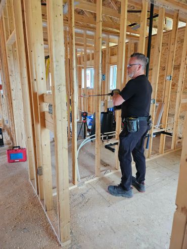 Worker drilling into wooden frame inside a house under construction.