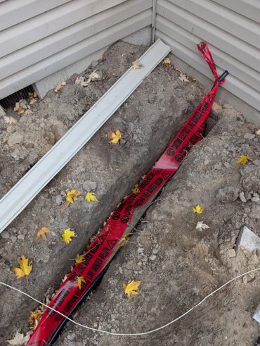 Trench near house with caution tape for buried electric line.