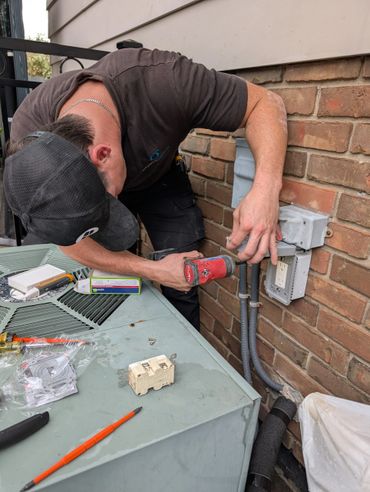 Technician installing an outdoor electrical outlet on a brick wall.