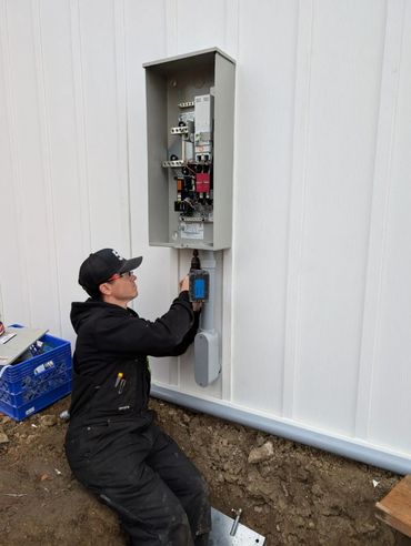 A worker installs electrical components in an outdoor panel on a white wall.