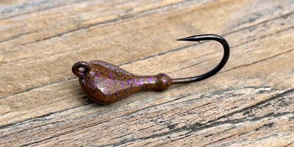 Close-up of a fishing jig with a brown glittery head on wooden surface.