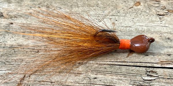 Brown fishing lure with hair-like tail on wooden surface.