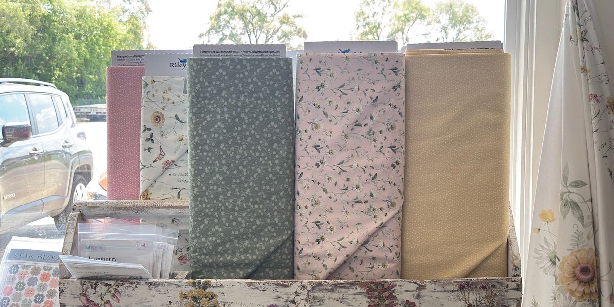 Various floral fabrics displayed on a wooden rack by a window.