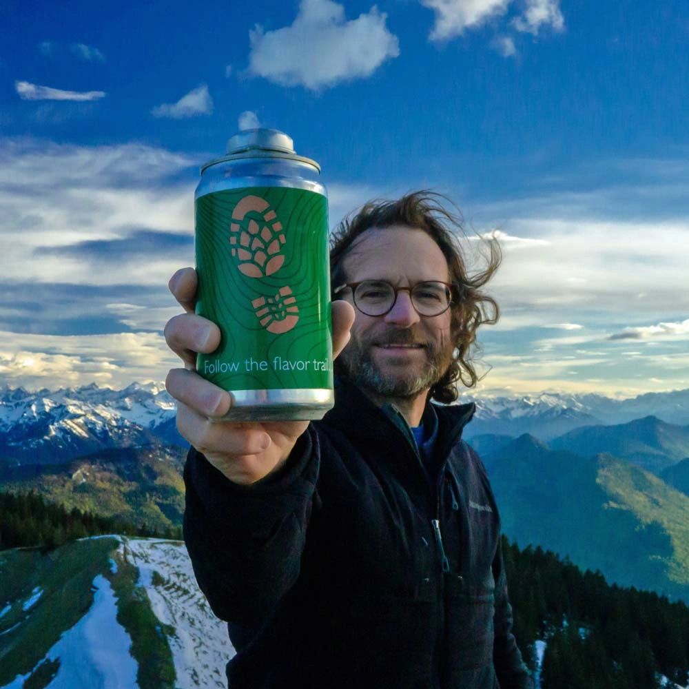 Paul Higgins on a mountaintop holding up a crowler of craft beer