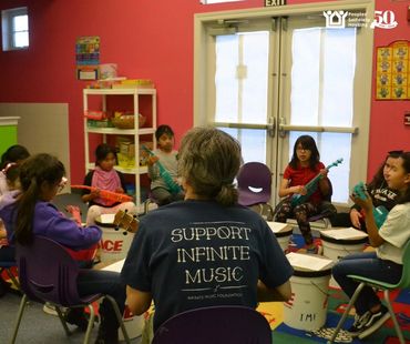 Ukulele and drum class with teacher wearing Support Infinite Music shirt.