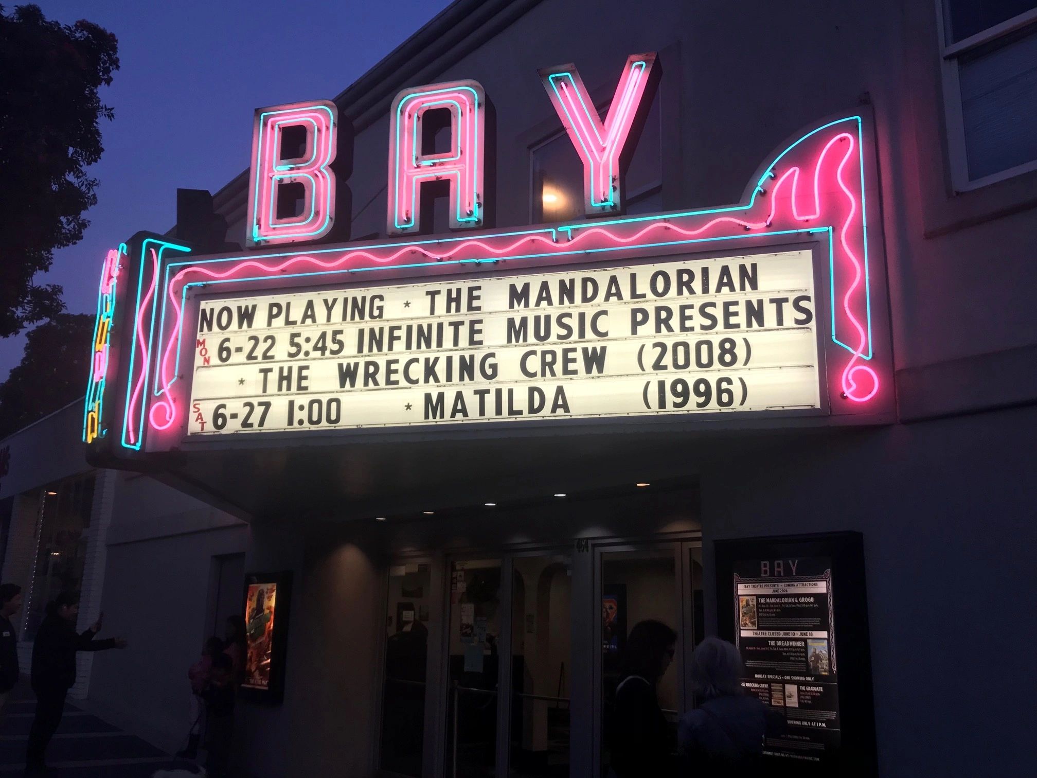 Neon-lit Bay Theatre marquee displaying movie showtimes and titles.