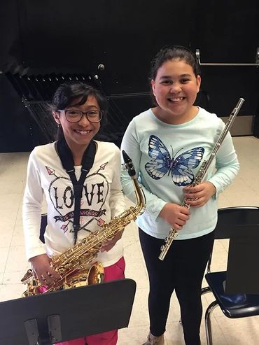Two smiling elementary school girls holding band instruments.