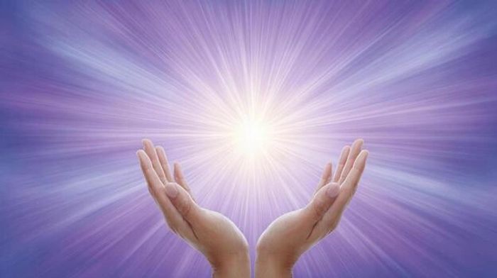 Hands cupped around a radiant light on a purple background.