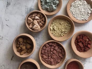 Various colorful powdered pigments and rocks in small clay bowls.
