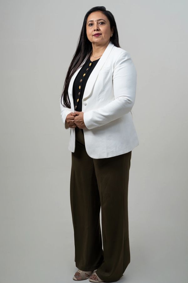 Confident woman in a white blazer and dark pants poses against a plain background.