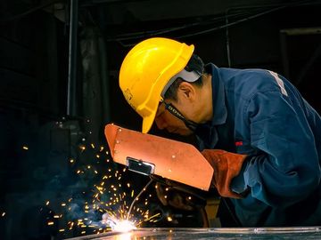 Worker welding metal with sparks flying in a dark workshop.