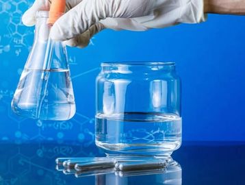Gloved hand holding laboratory glassware with clear liquid against a blue scientific background.