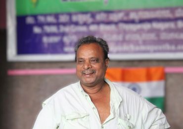 Smiling man in a white shirt with Indian flag in background.