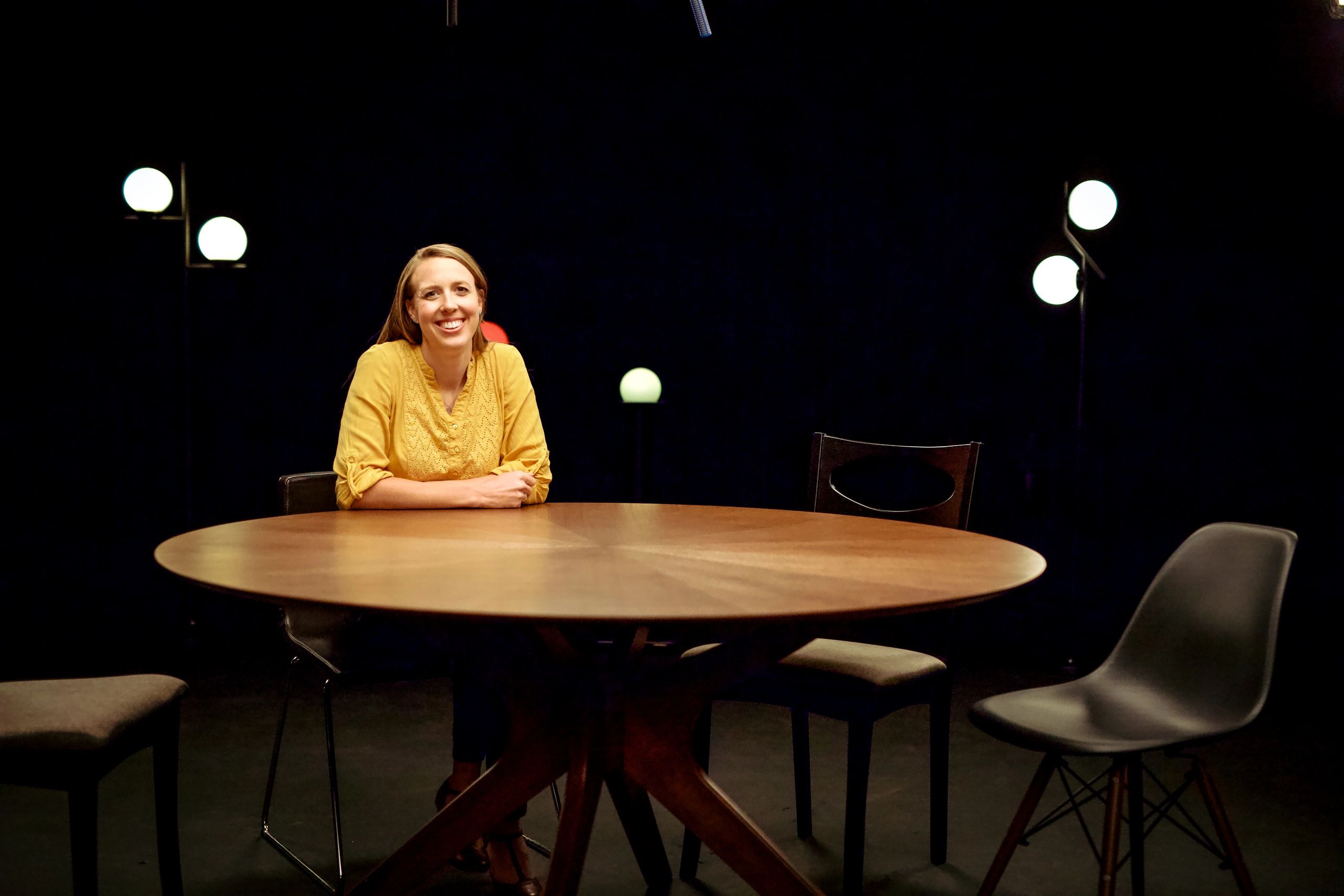 Hailey Jones sits "AT THE TABLE" smiling wearing yellow