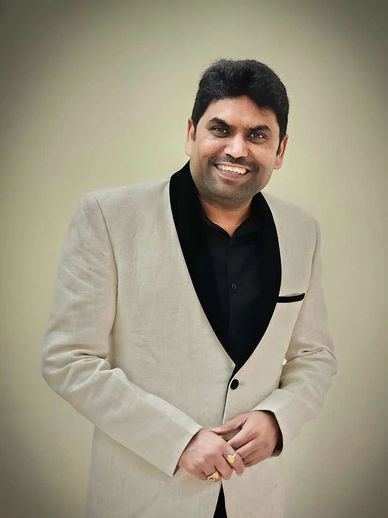 Man in beige blazer smiling.