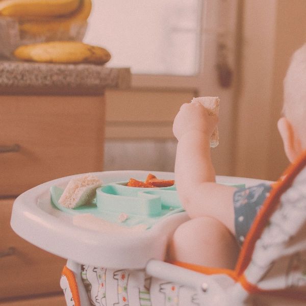 Baby eating food while sitting in a highchair.