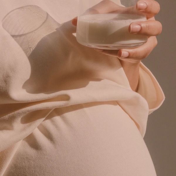 Person holding a glass of milk with a beige pullover.