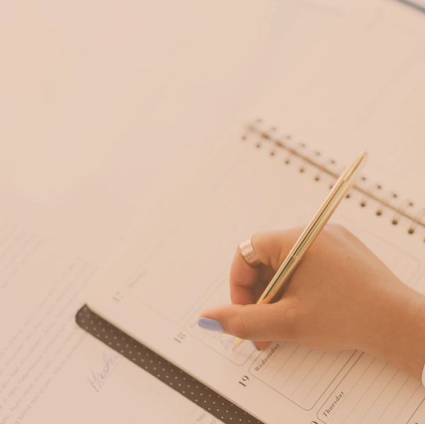 Hand writing in a notebook with a gold pen.