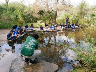a group of kids around the pond learning