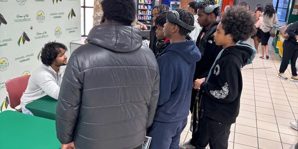 Students gather around a booth promoting Kentucky State University in a school hallway.