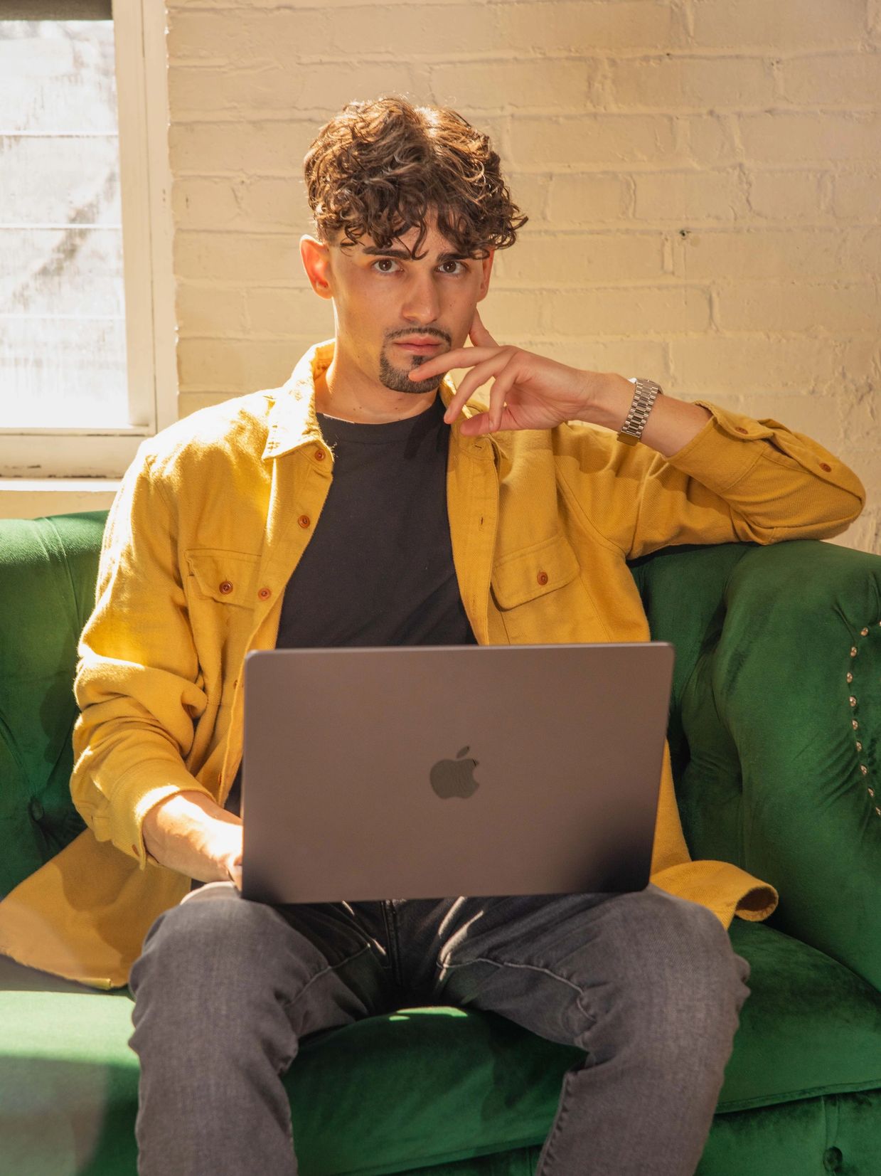 Man in yellow shirt using a laptop on a green sofa.