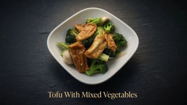 Tofu with mixed vegetables served in a white bowl on a dark background.
