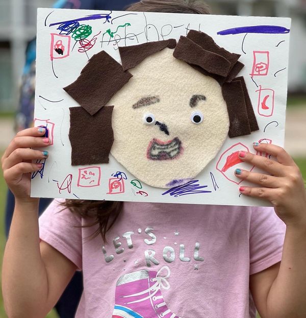 A young white girl holds a self portrait she made up in front of her face.
