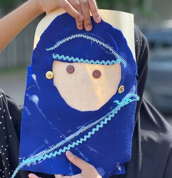 A young muslim girl holds a self portrait she made up in front of her face.