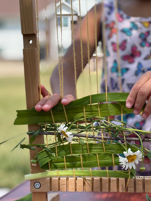 Image of a young girl's hands as she is creating a nature weaving