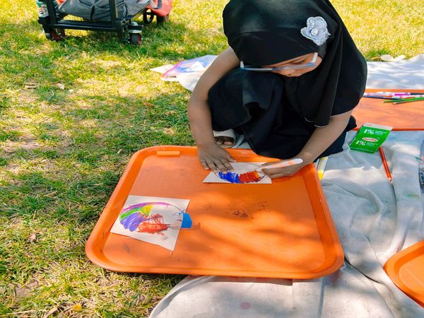 A child in a black outfit painting on a paper outdoors.