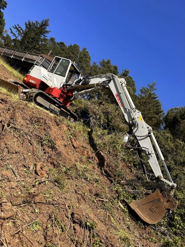 Excavator working on a sloped terrain under a clear blue sky.